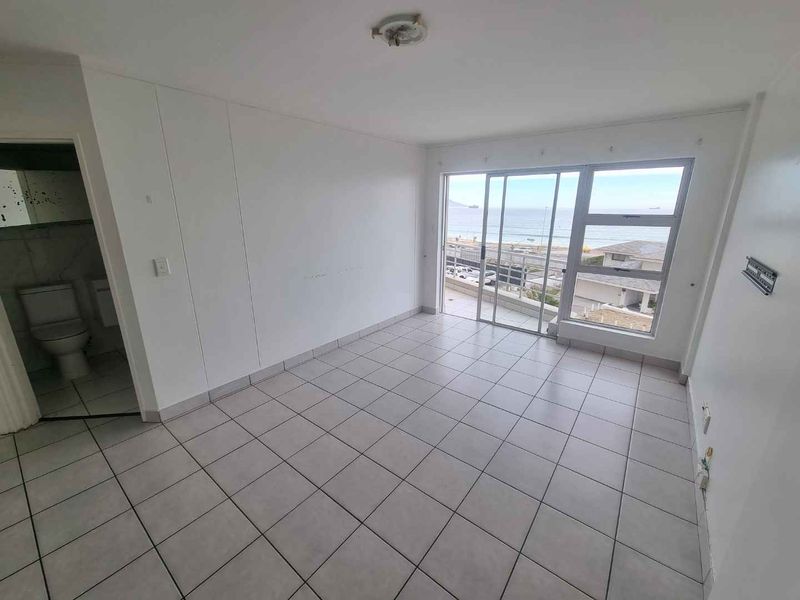 An empty living room featuring tiled flooring, sliding glass doors with ocean views, and direct access to an adjacent bathroom.