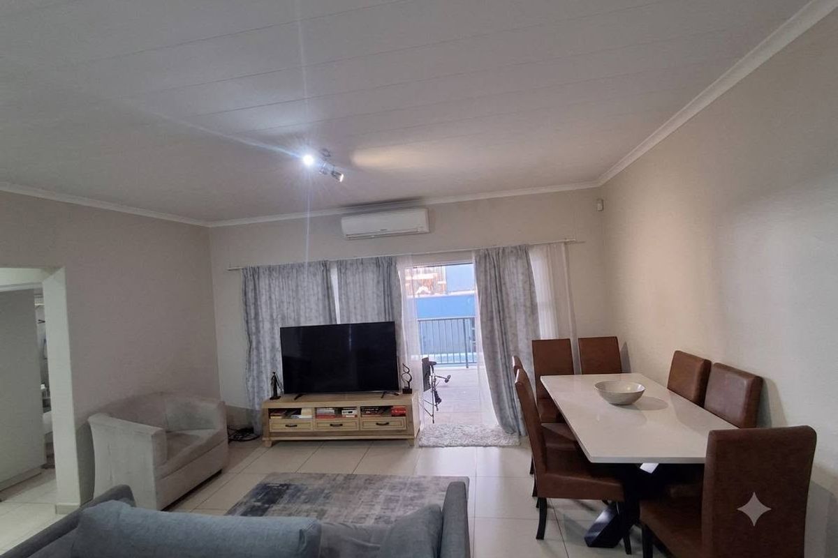 An open-plan living and dining area featuring tiled flooring, a split-system air conditioner, and direct access to a balcony through sliding glass doors.