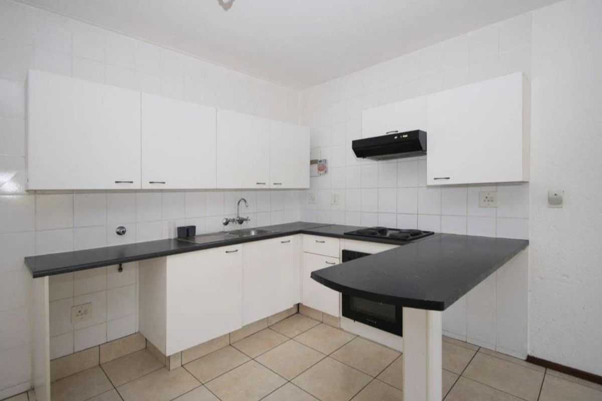 A functional kitchen featuring white cabinetry, black countertops, a built-in oven with gas hob, and tiled finishes throughout.
