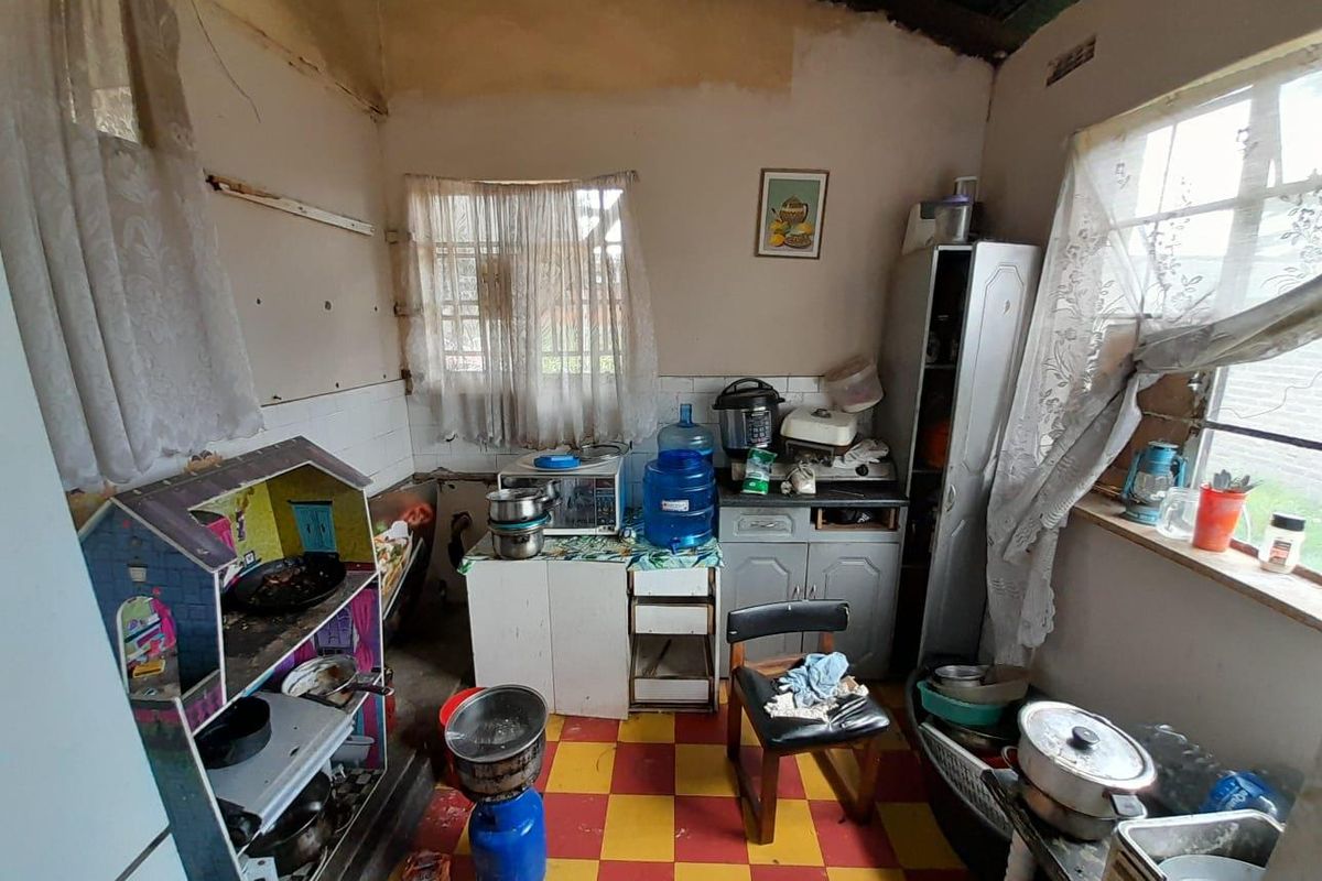 A dated kitchen area featuring basic cabinetry, tiled flooring, and exposed wall surfaces, requiring significant renovation and modernization to improve functionality and aesthetic appeal.