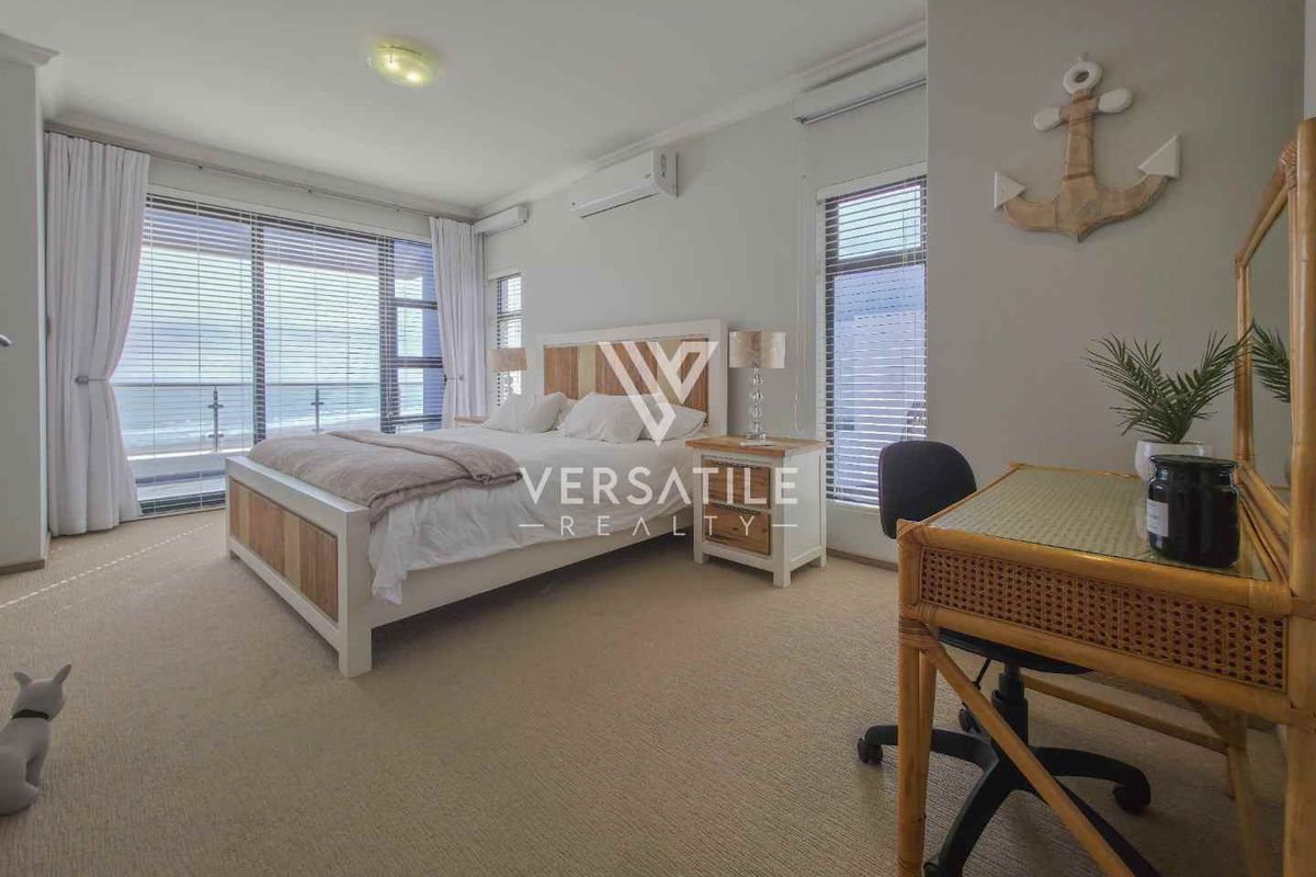Spacious bedroom featuring large windows, sliding glass doors leading to a balcony, and a wall-mounted air conditioning unit.
