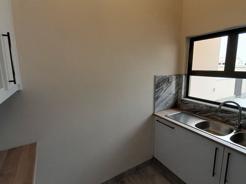 A clean, modern scullery featuring built-in cabinetry, a stainless steel double sink with mixer tap, and a stylish marble-look splashback.