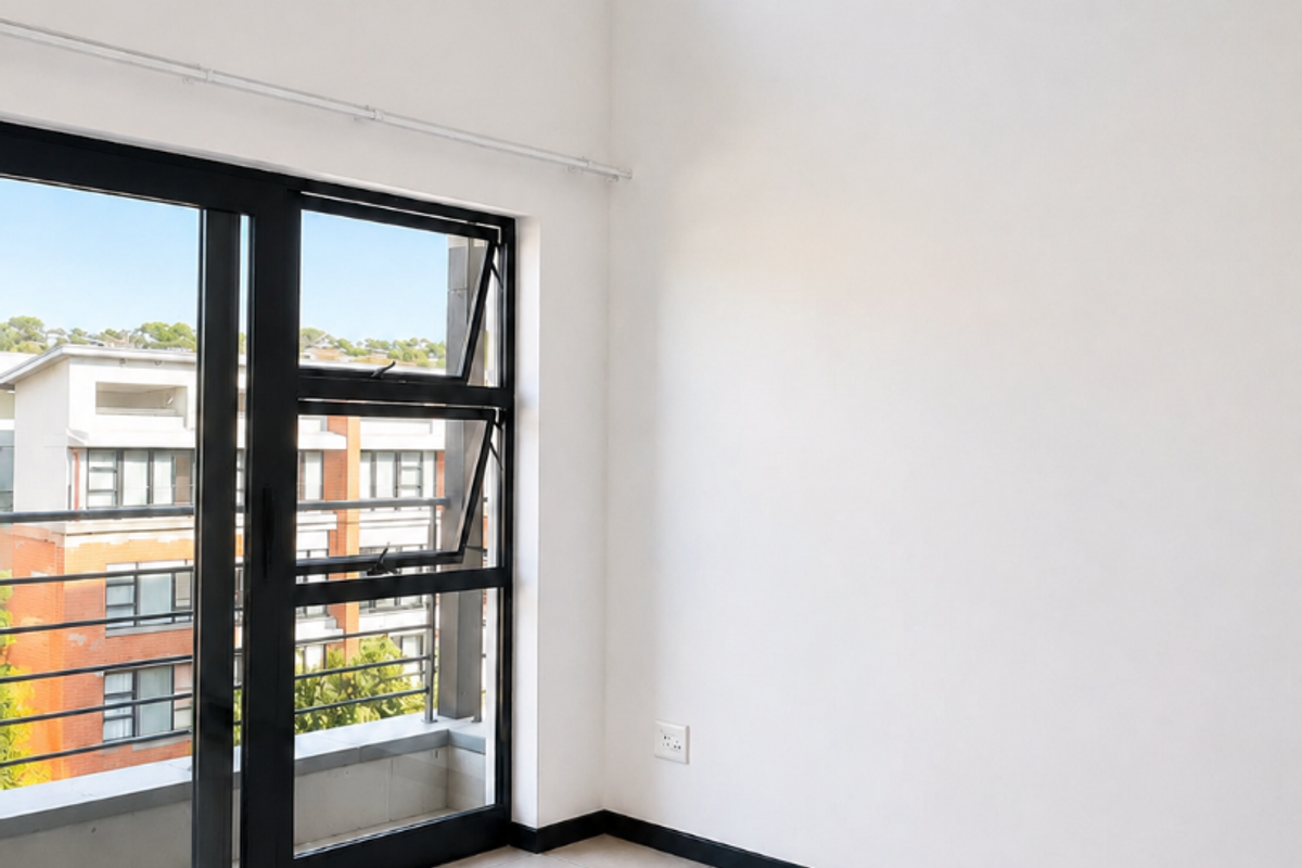 A bright, empty living area featuring double volume ceilings, large aluminium sliding doors leading to a balcony, and neutral tiled flooring.