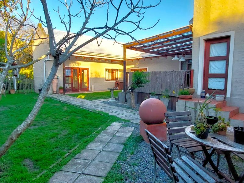 A rear garden view featuring a paved walkway, a covered patio area with a timber pergola, and a well-maintained lawn.