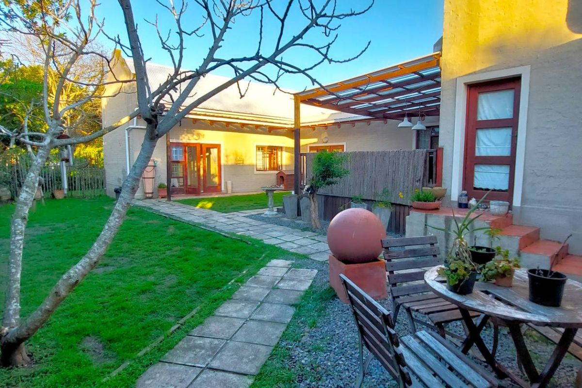 A rear garden view featuring a paved walkway, a covered patio area with a timber pergola, and a well-maintained lawn.