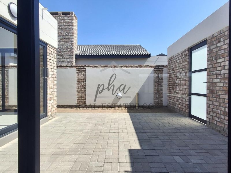 A modern, paved outdoor courtyard area featuring exposed brick walls, integrated wall lighting, and access to the main dwelling via large sliding glass doors.