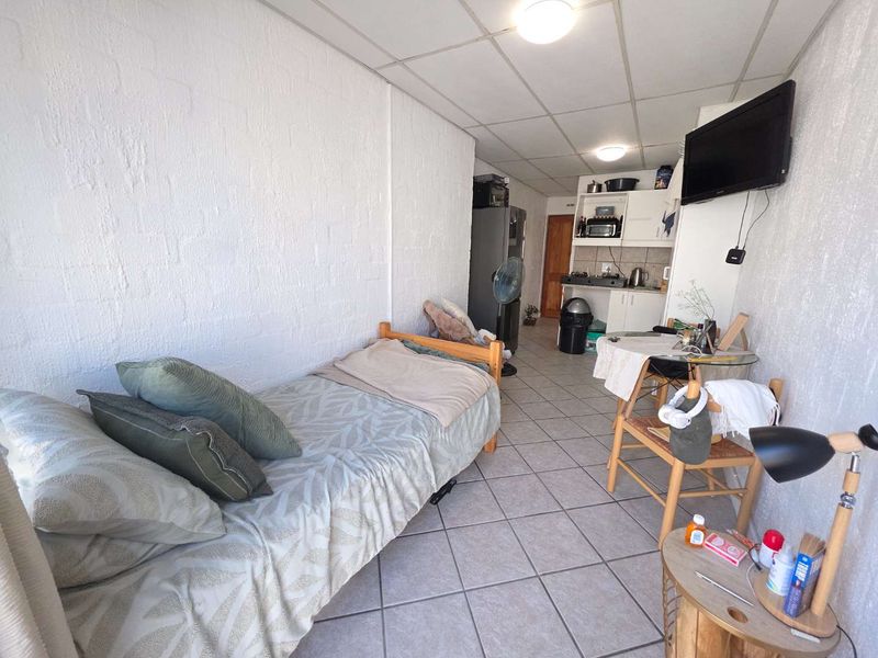 Compact open-plan studio apartment featuring tiled flooring, a drop ceiling, and a functional kitchenette with built-in cabinetry and cooking appliances.