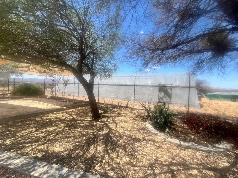A spacious outdoor garden area featuring established trees, stone garden edging, and a large enclosed structure with electric fencing.