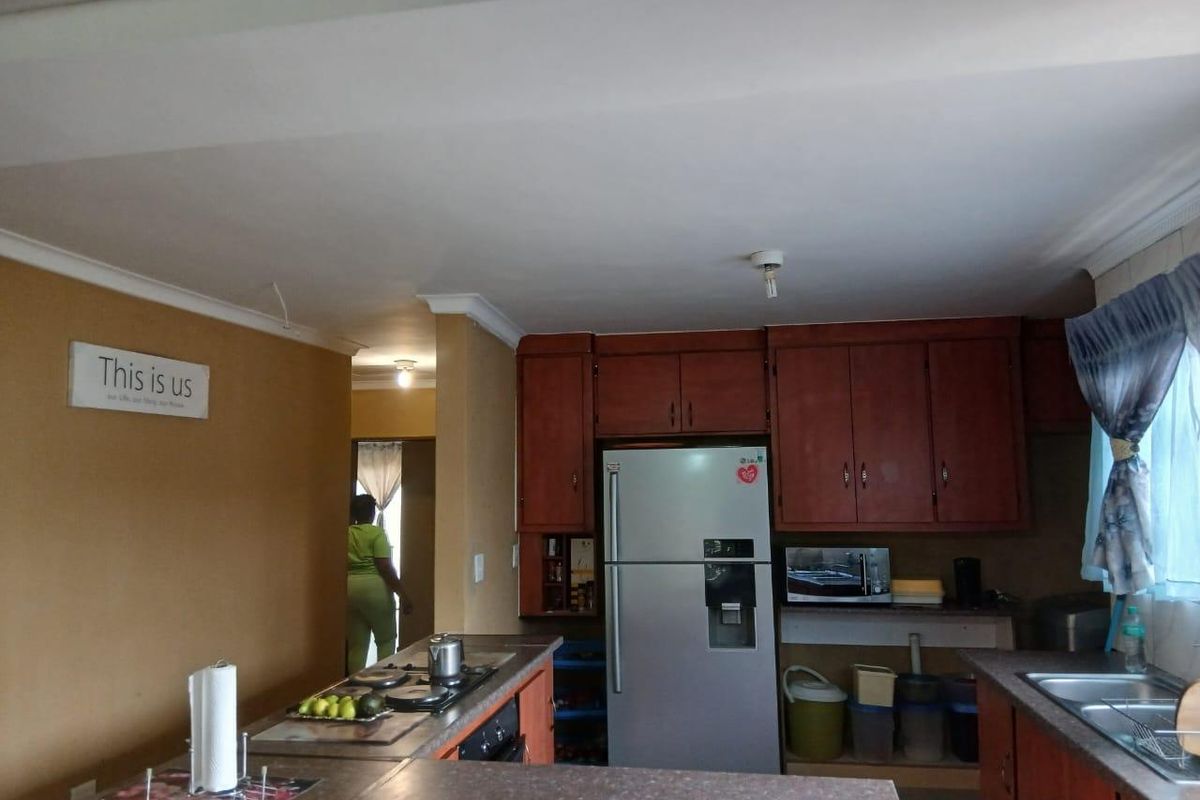 A functional kitchen featuring wooden cabinetry, a built-in hob, and a double sink, with an open-plan layout connecting to the adjacent living area.