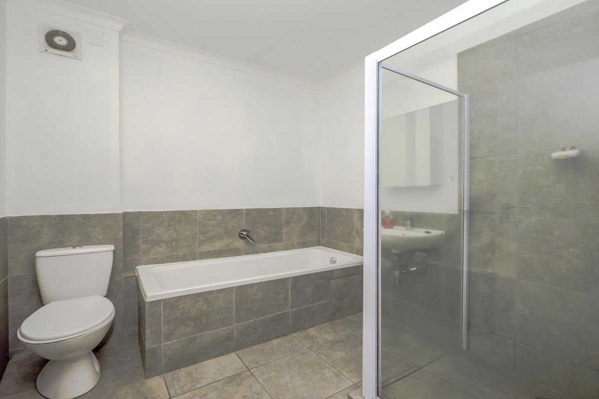 A clean, functional bathroom featuring a separate bathtub and shower enclosure with neutral grey tiling and white sanitaryware.
