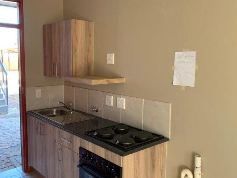 A compact kitchen featuring wood-look cabinetry, a built-in oven and hob, tiled backsplash, and tiled flooring with direct access to the exterior.