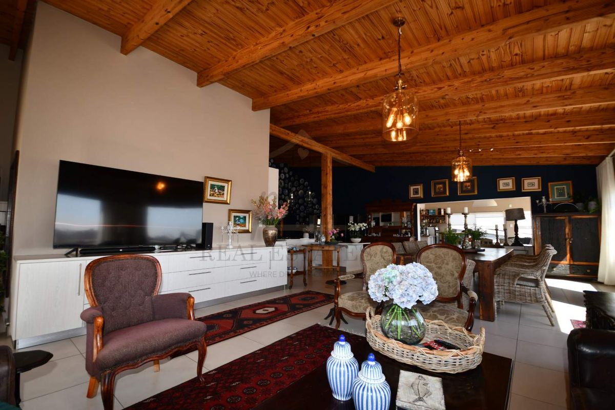 Spacious open-plan living and dining area featuring high exposed timber beam ceilings, tiled flooring, and integrated cabinetry.