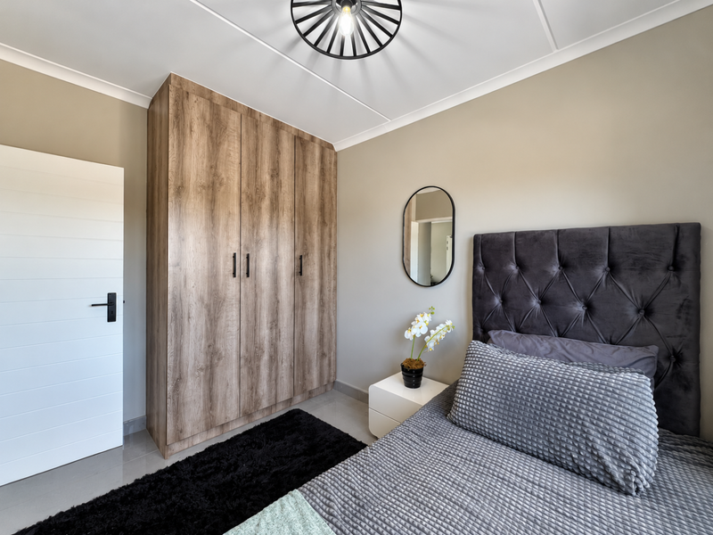 A well-maintained bedroom featuring neutral wall tones, tiled flooring, and a large wood-finish built-in wardrobe providing ample storage space.