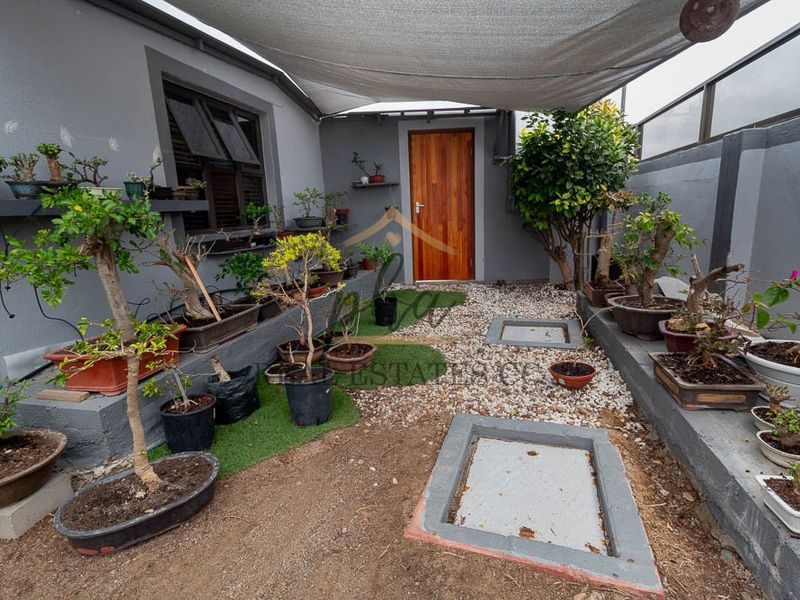 A private rear courtyard area featuring a shade sail, raised concrete planters, and a timber entrance door.