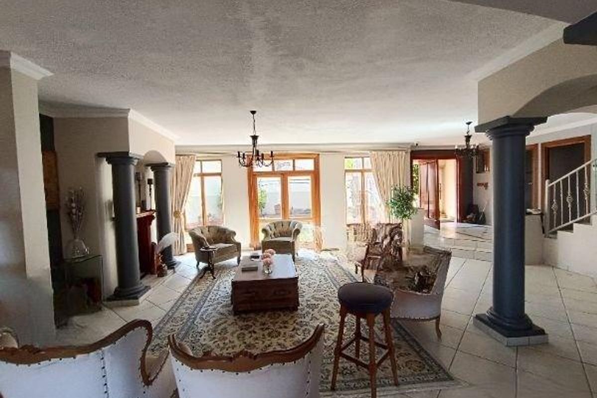 Spacious open-plan living area featuring decorative columns, tiled flooring, and large windows providing natural light, with an adjacent staircase.