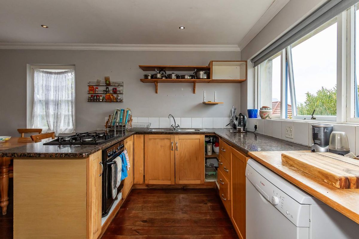 A functional kitchen featuring timber cabinetry, granite-style countertops, a gas hob, and integrated dishwasher, with natural light from the adjacent window.