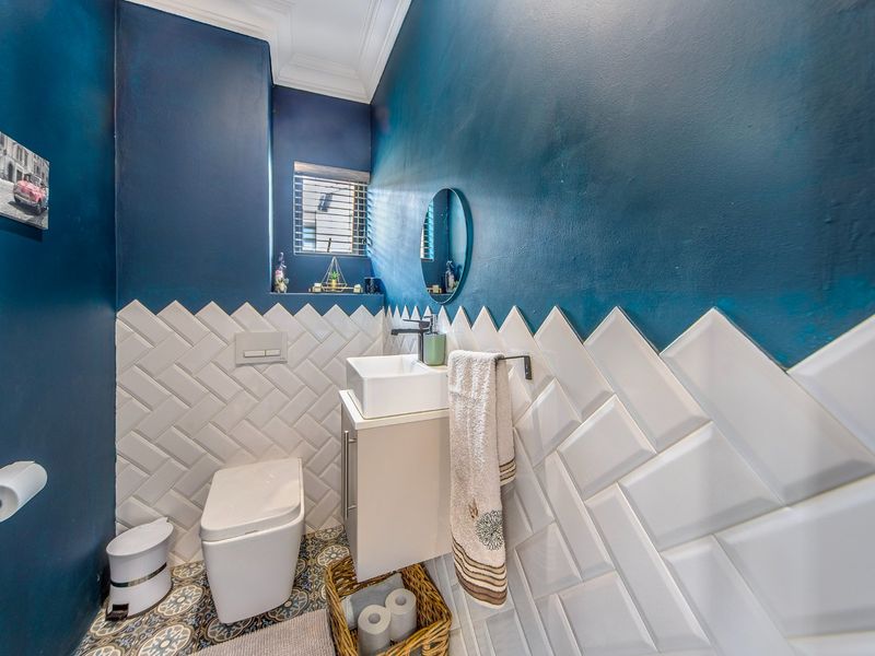 A modern guest bathroom featuring bold blue walls, white herringbone tiling, a wall-mounted toilet with concealed cistern, and a compact vanity basin.
