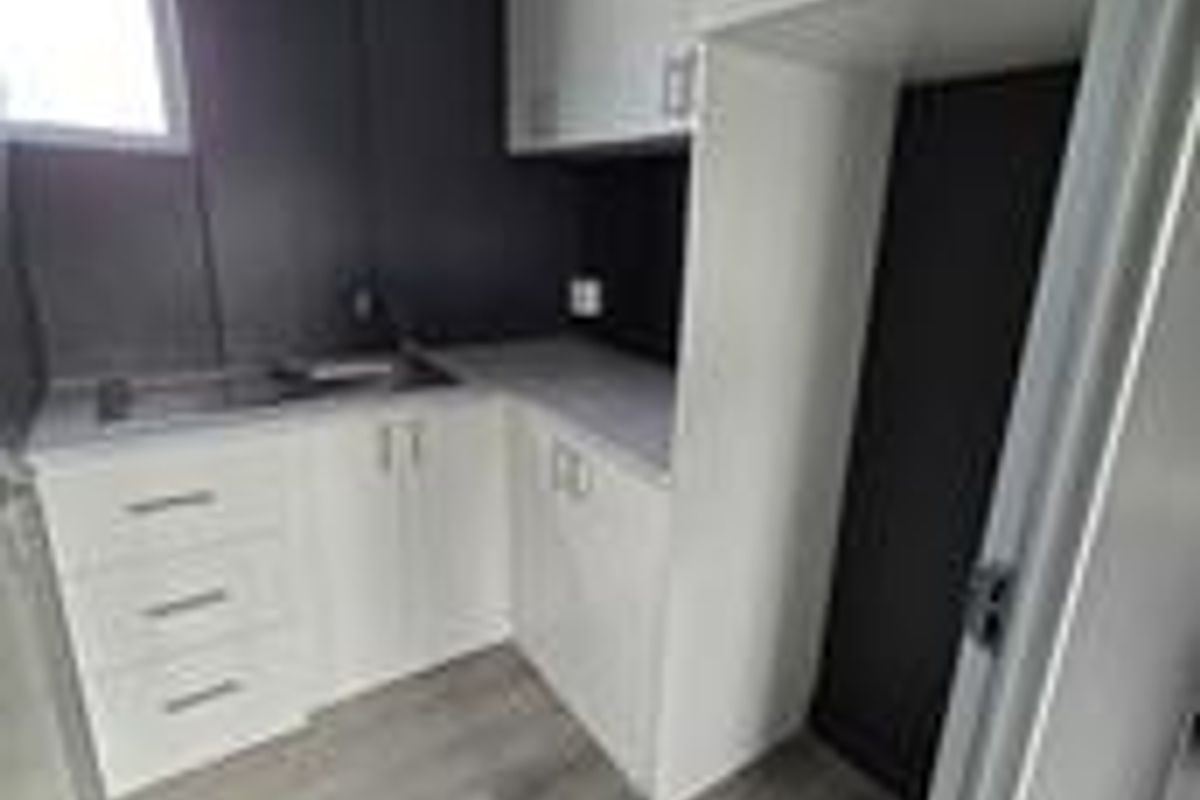 A compact office kitchenette featuring modern white cabinetry, a stainless steel sink, and wood-look flooring.