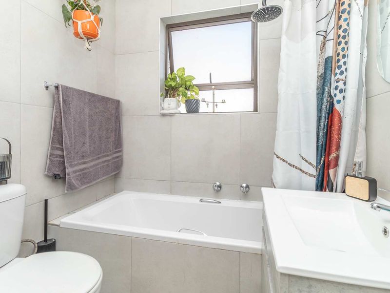 A modern bathroom featuring a built-in bathtub with an overhead shower, a vanity basin, and neutral wall tiling.