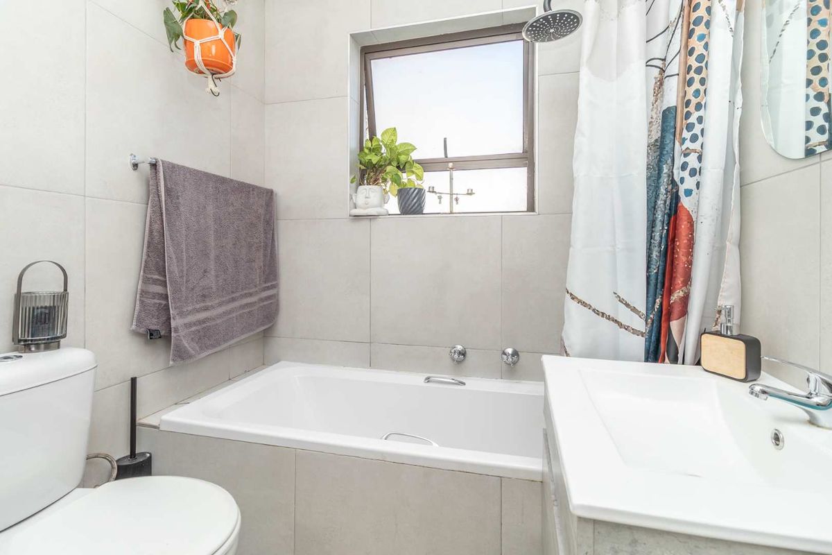 A modern bathroom featuring a built-in bathtub with an overhead shower, a vanity basin, and neutral wall tiling.