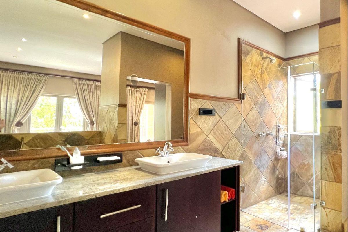 A well-appointed bathroom featuring a double vanity with stone countertop, large framed mirror, and a spacious walk-in shower with natural stone tiling.