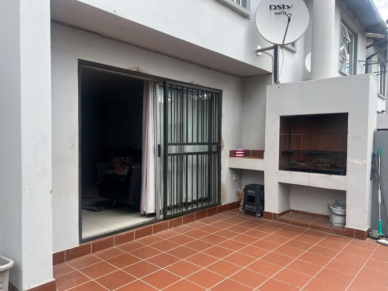Outdoor patio area featuring a built-in braai, tiled flooring, and a sliding door with security gate providing access to the interior living space.