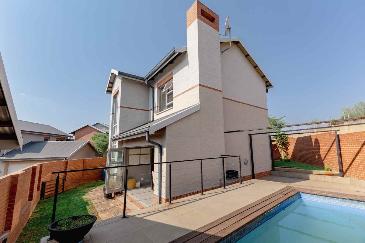 Rear view of the townhouse featuring a private swimming pool, paved patio area, and a brick boundary wall.