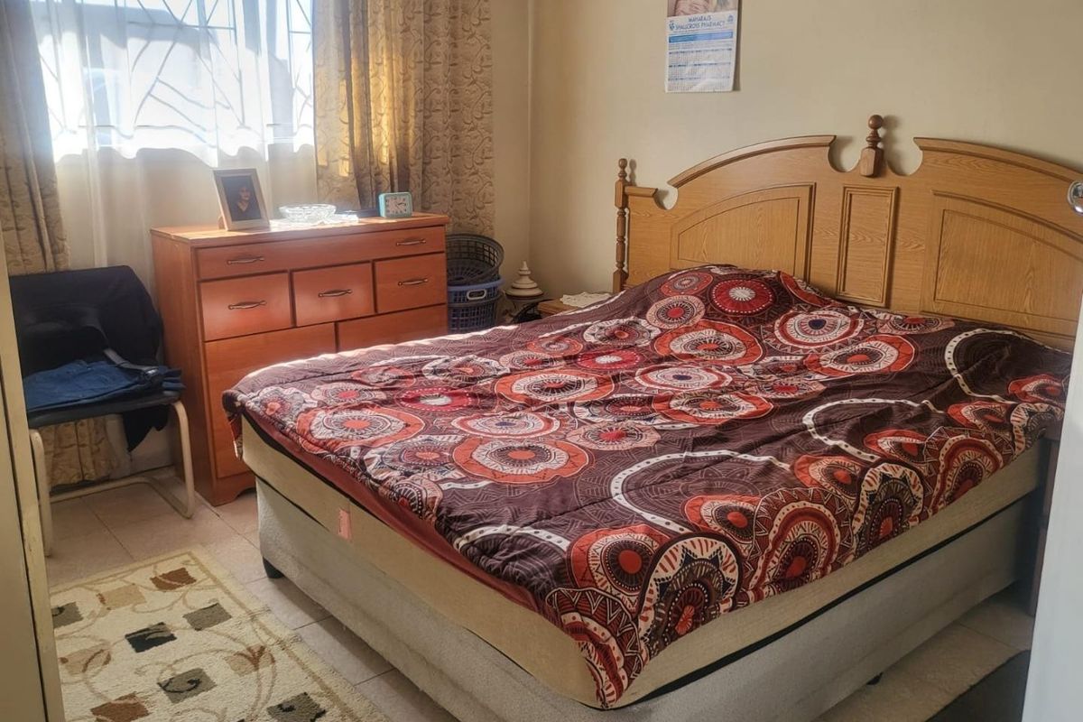 A functional bedroom featuring tiled flooring and a security gate on the window, providing a standard living space.