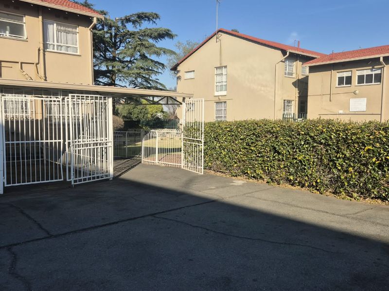 Exterior view of the townhouse complex featuring a paved driveway, secure gated carport, and established perimeter hedging.