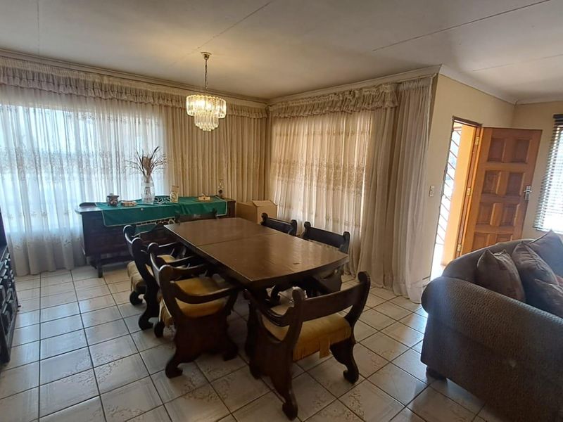 A dining room featuring tiled flooring, ceiling cornices, and natural light through large windows with curtains.
