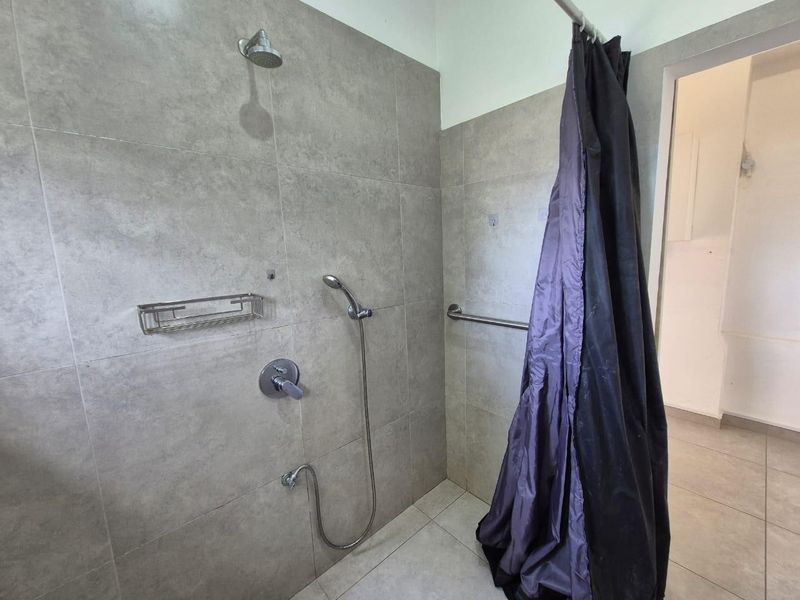 A modern bathroom shower area featuring large format grey wall tiles, a dual shower head system, and a safety grab rail.