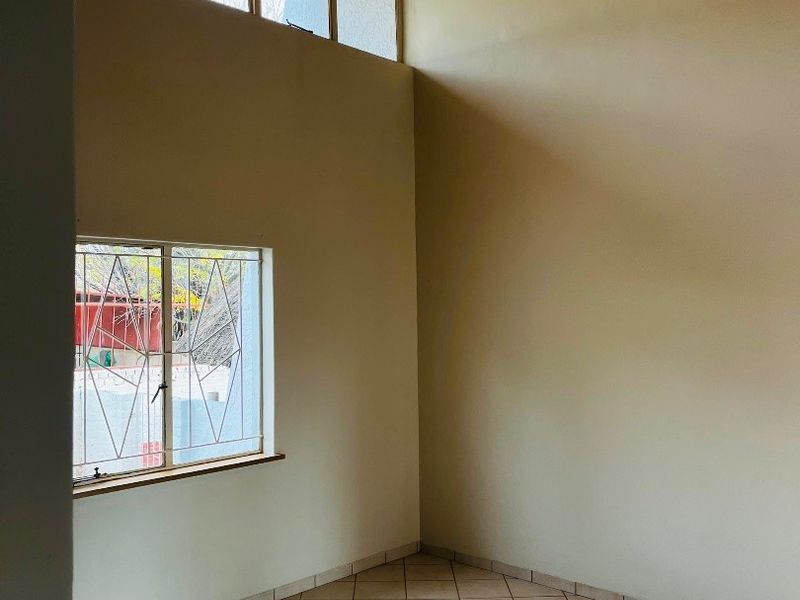 An empty living area featuring a high timber-clad vaulted ceiling, tiled flooring, and clerestory windows that provide ample natural light.