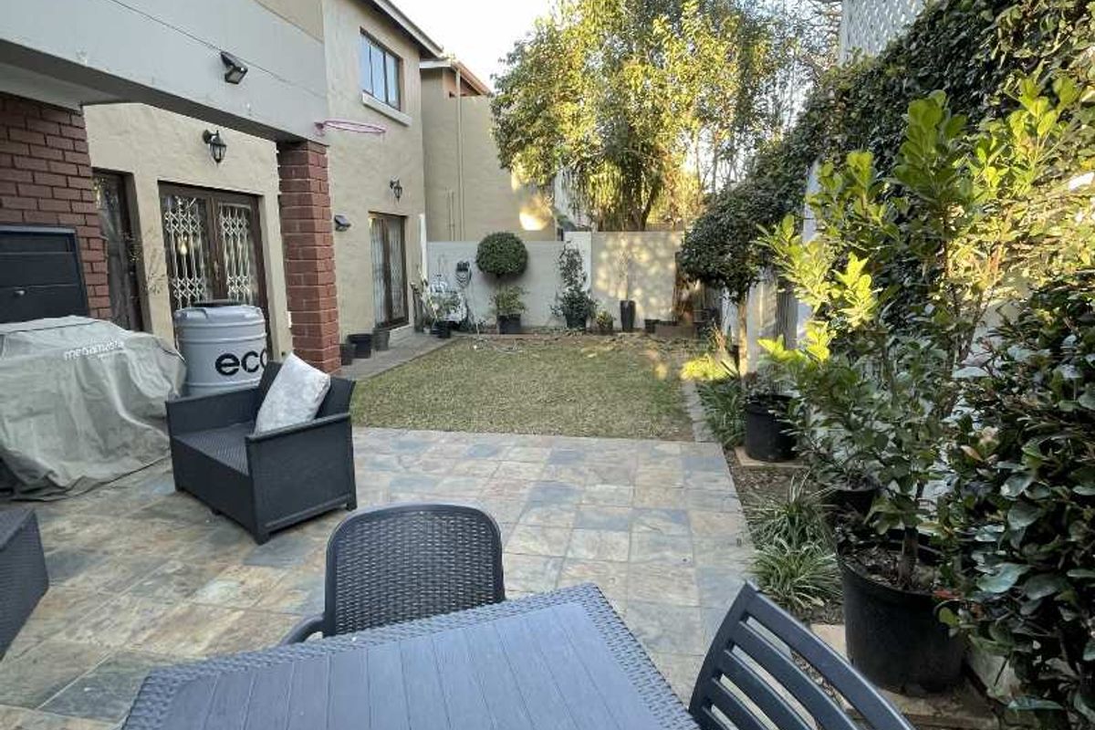 A private rear garden featuring a paved patio area, a small lawn, and established boundary walls with trellis fencing.