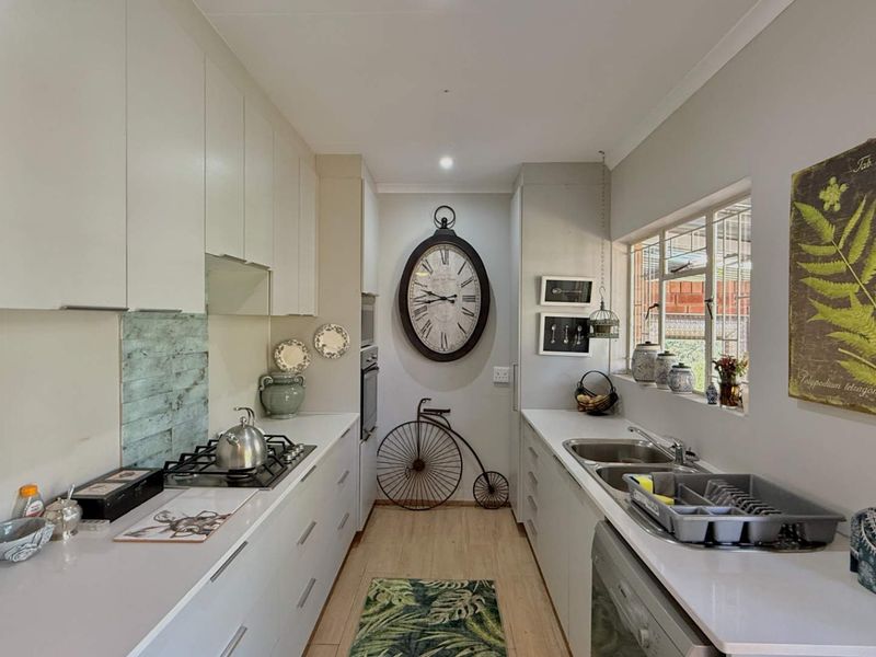 A functional galley-style kitchen featuring white cabinetry, a gas hob, built-in oven, and a double sink with ample counter space.