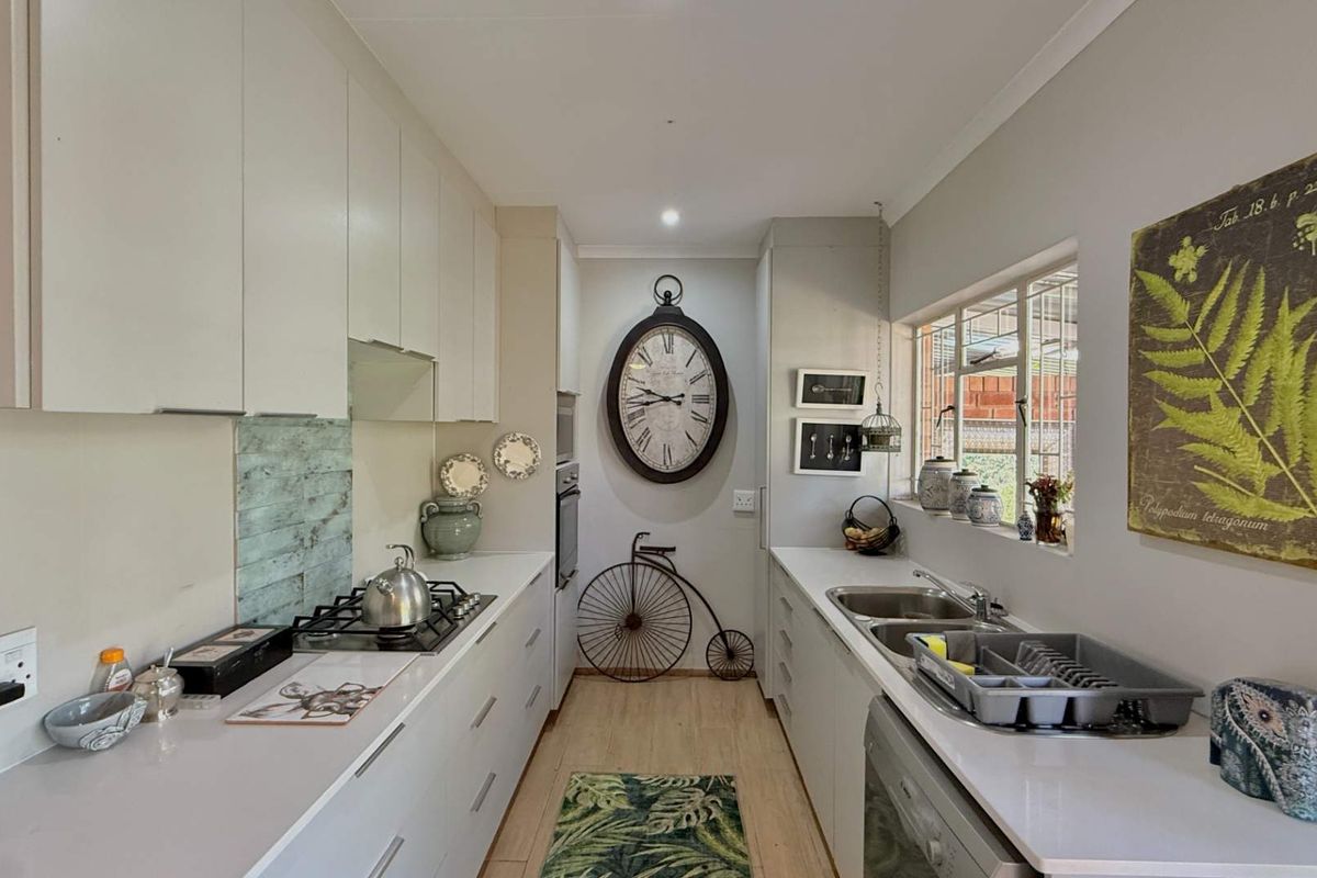 A functional galley-style kitchen featuring white cabinetry, a gas hob, built-in oven, and a double sink with ample counter space.