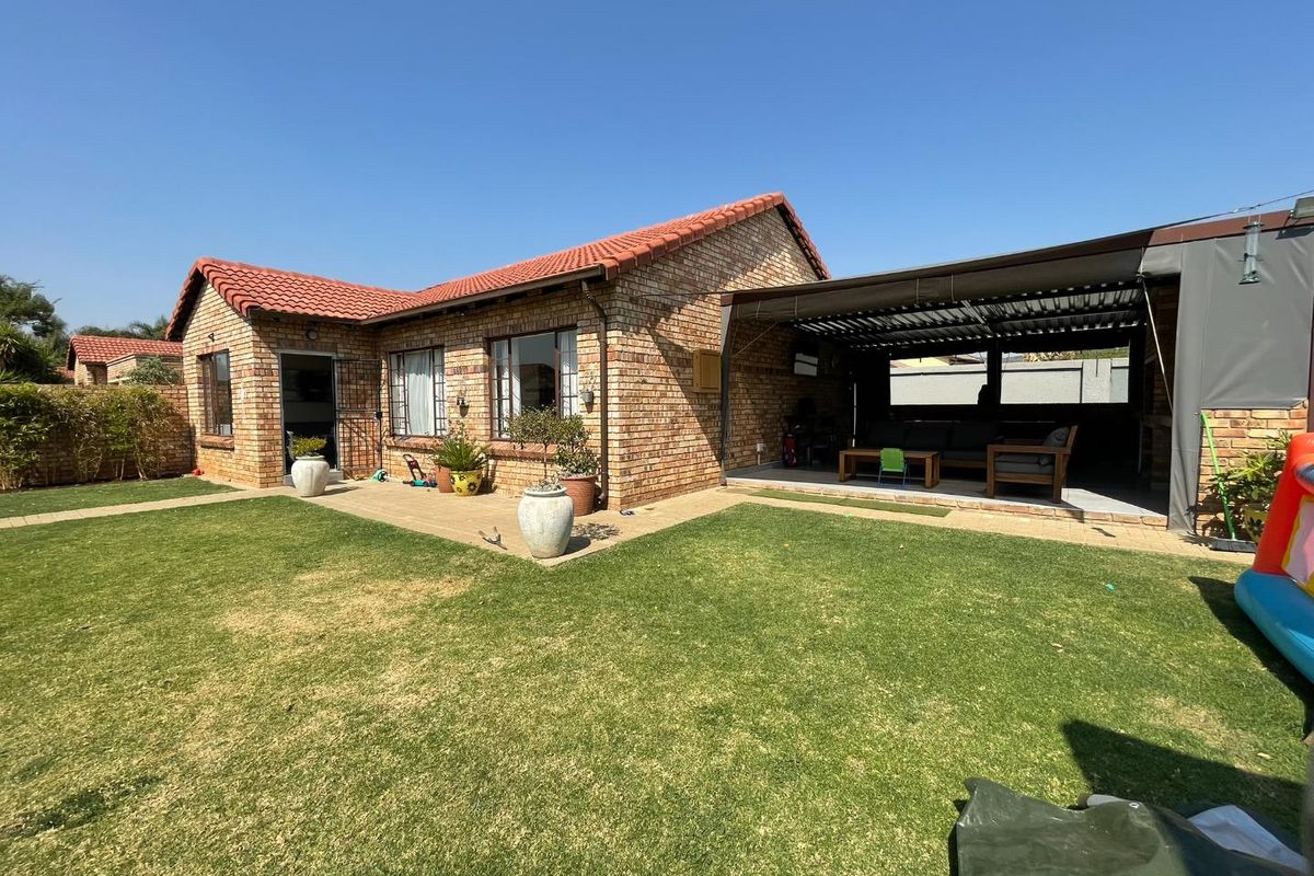 Rear view of the townhouse featuring a face-brick facade, terracotta roof tiles, a paved patio area, and a well-maintained garden.