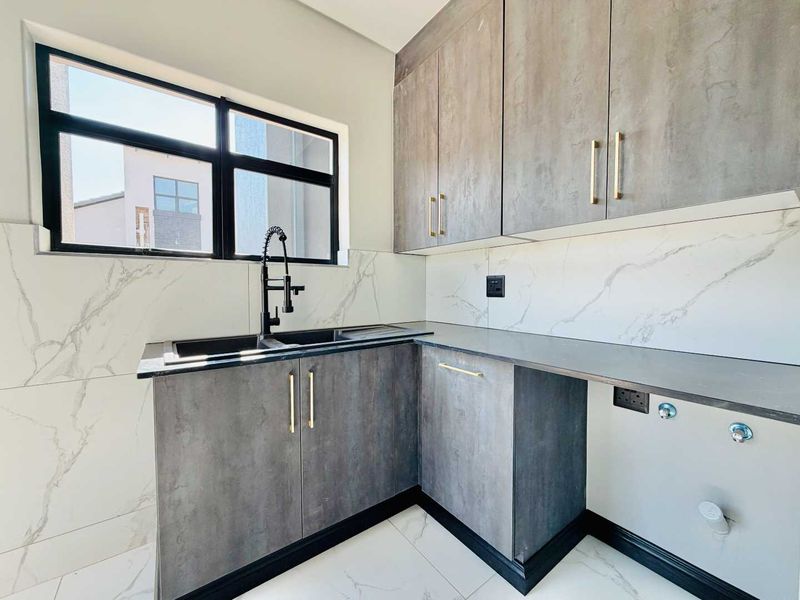 Modern laundry room featuring sleek grey cabinetry, marble-look wall tiles, a black sink with a gooseneck tap, and dedicated plumbing connections for appliances.