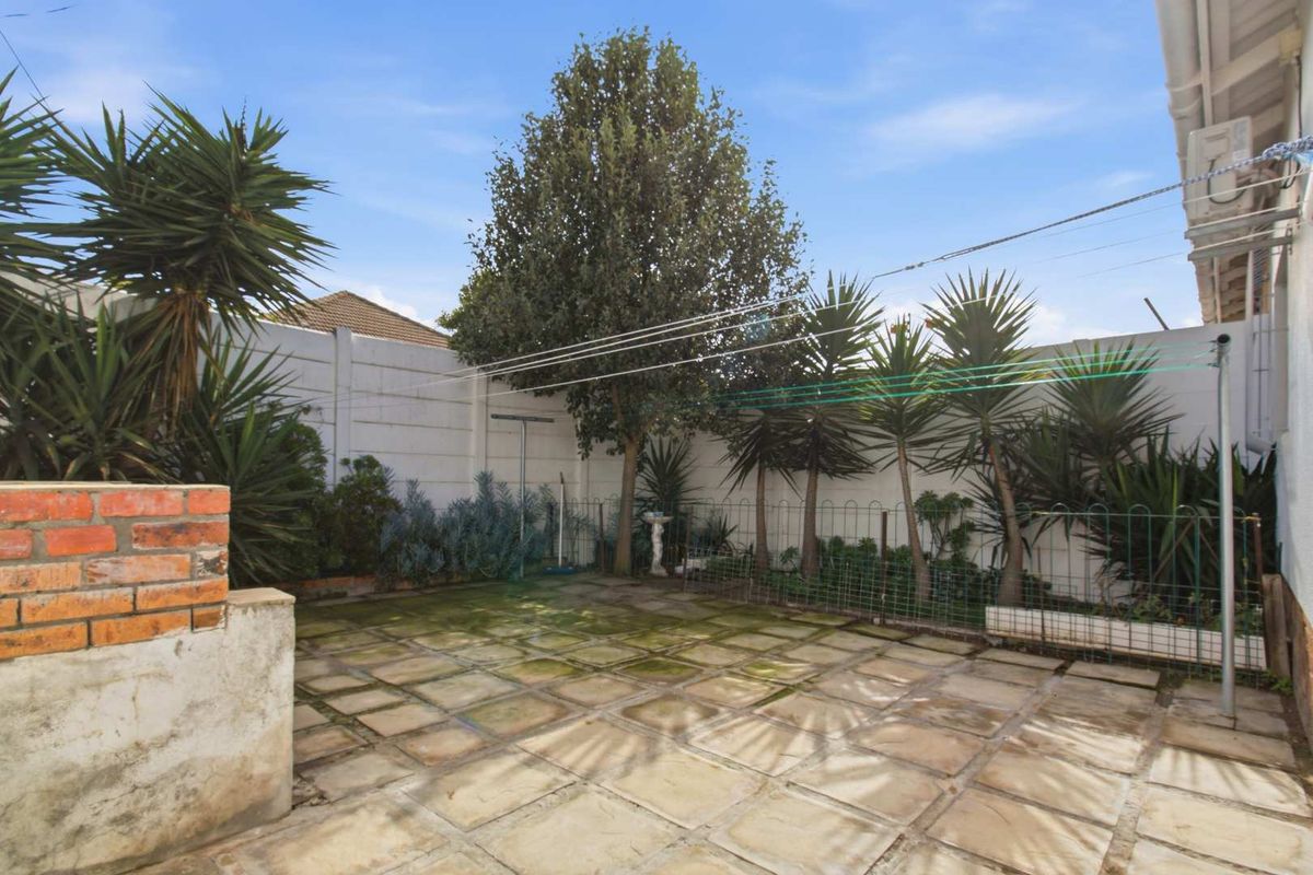 A rear courtyard featuring paved flooring, boundary walls, and a clothesline, requiring maintenance to address moss and surface staining.