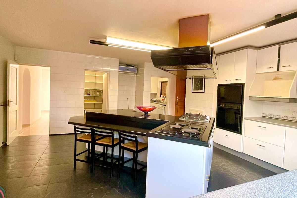 Spacious kitchen featuring a central island with a built-in gas hob, integrated oven, extractor fan, and ample white cabinetry with tiled walls.