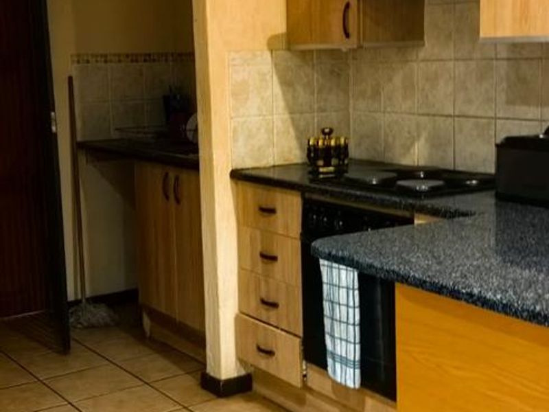 Functional kitchen featuring laminate cabinetry, granite countertops, built-in oven, and electric hob with extractor fan, finished with ceramic floor tiles.