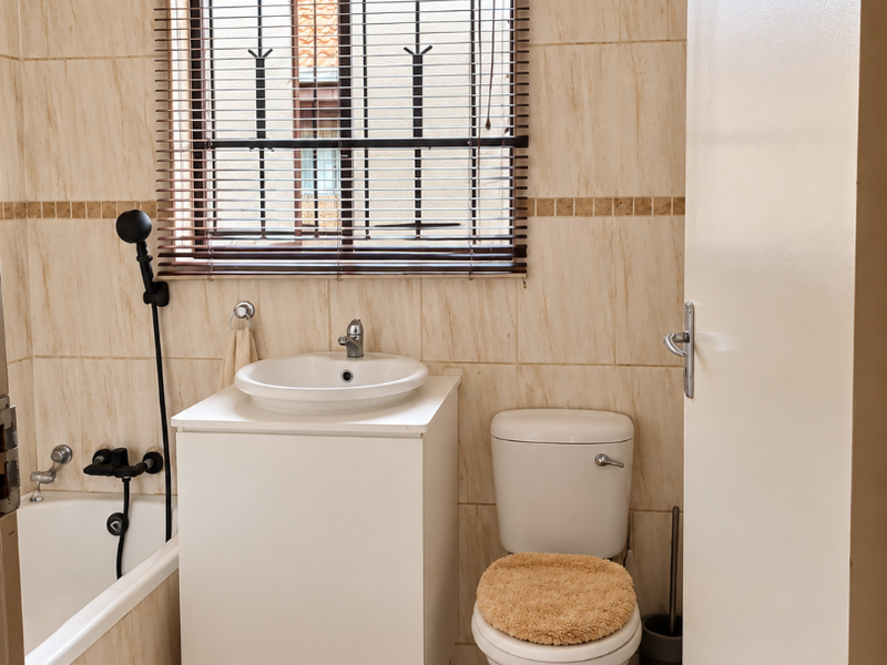 A functional bathroom featuring a built-in bathtub, a modern vessel sink vanity, and a standard toilet, finished with neutral wall and floor tiles.
