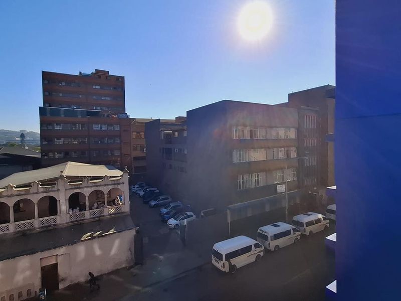An elevated urban view overlooking surrounding apartment buildings, a parking area, and a street with parked vehicles.
