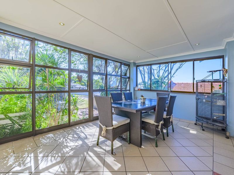 A bright, enclosed patio area featuring large glass windows, tiled flooring, and recessed lighting, offering a comfortable space for indoor-outdoor living.