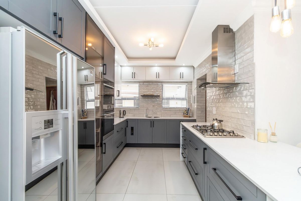 Modern galley-style kitchen featuring sleek grey cabinetry, white stone countertops, subway tile backsplash, built-in oven, and stainless steel gas cooktop with extractor fan.