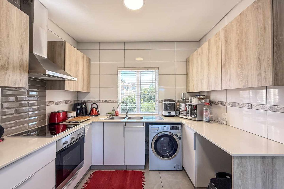 Modern kitchen featuring light wood-grain cabinetry, stone countertops, integrated oven, electric hob, extractor fan, and a built-in space for a washing machine.