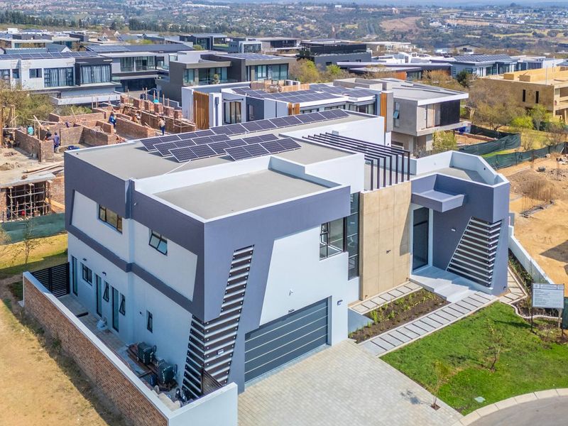Aerial view of a modern contemporary house featuring solar panels, a double garage, and a paved driveway in a residential estate.