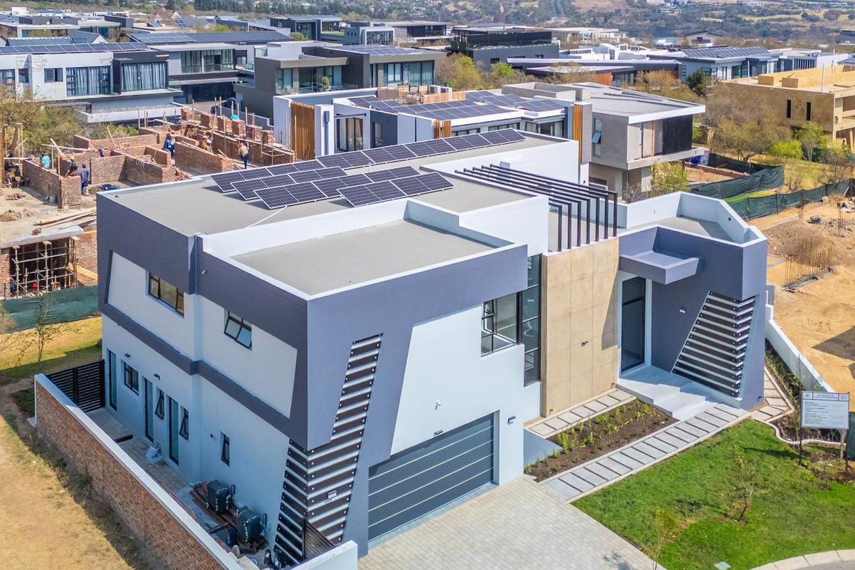 Aerial view of a modern contemporary house featuring solar panels, a double garage, and a paved driveway in a residential estate.