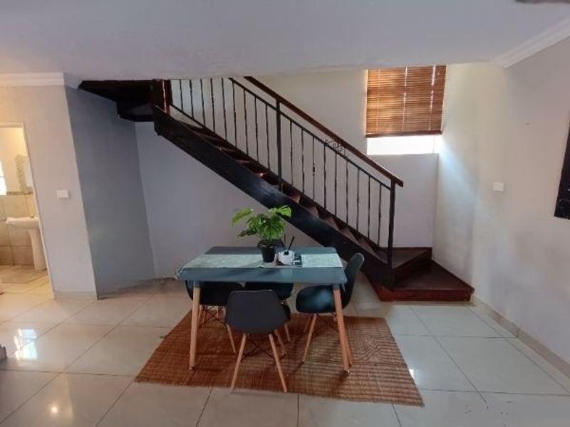 Open plan living area featuring a prominent staircase with a wrought iron balustrade and neutral tiled flooring.