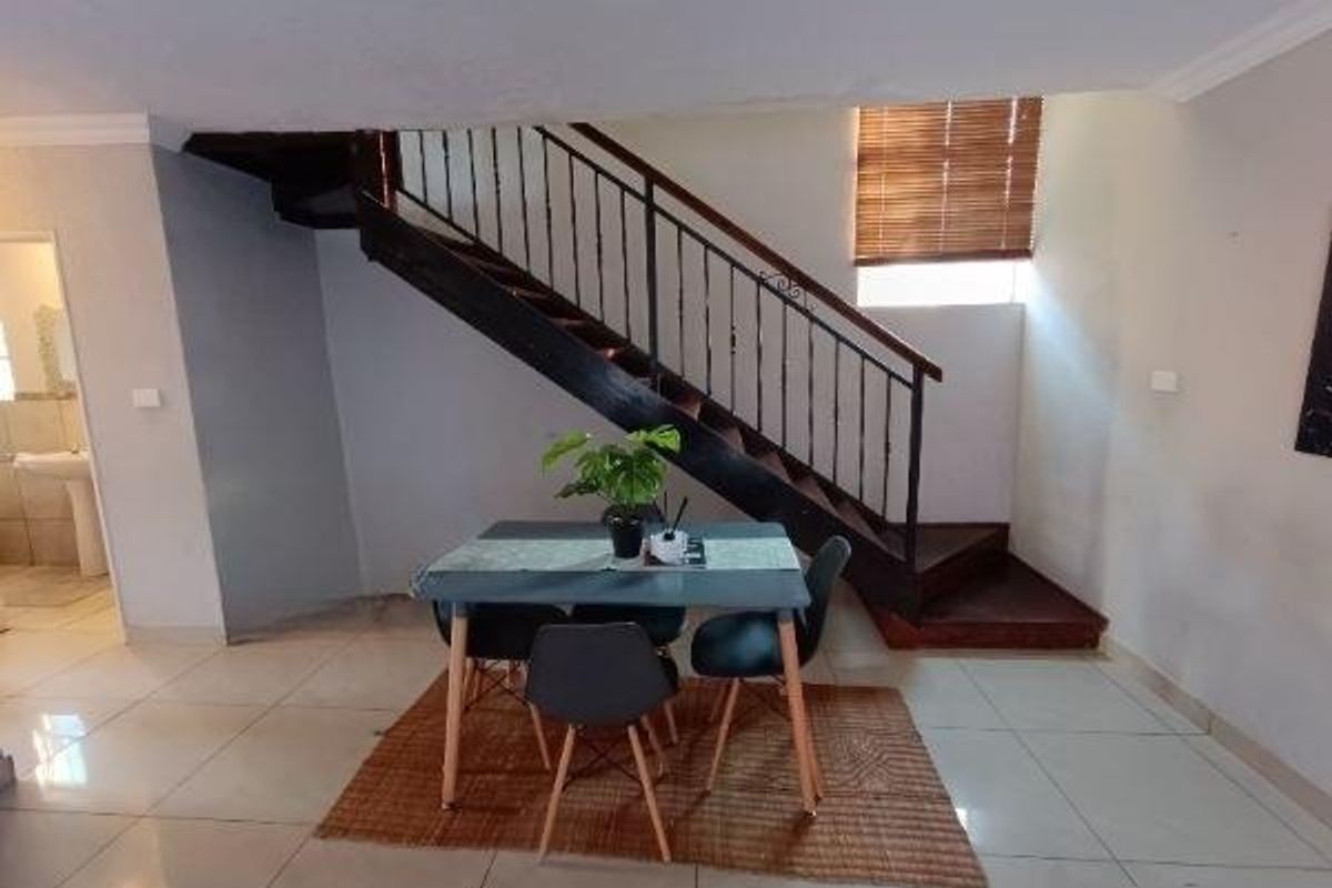 Open plan living area featuring a prominent staircase with a wrought iron balustrade and neutral tiled flooring.