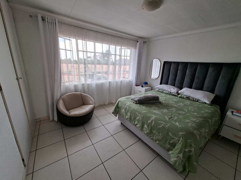 A bedroom featuring tiled flooring, a built-in cupboard, and a large window providing natural light.